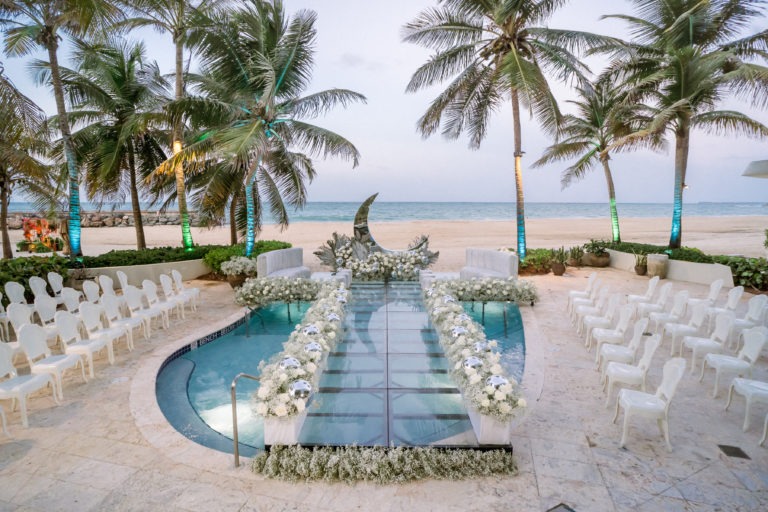 A glass walkway over a pool leading to a wedding altar