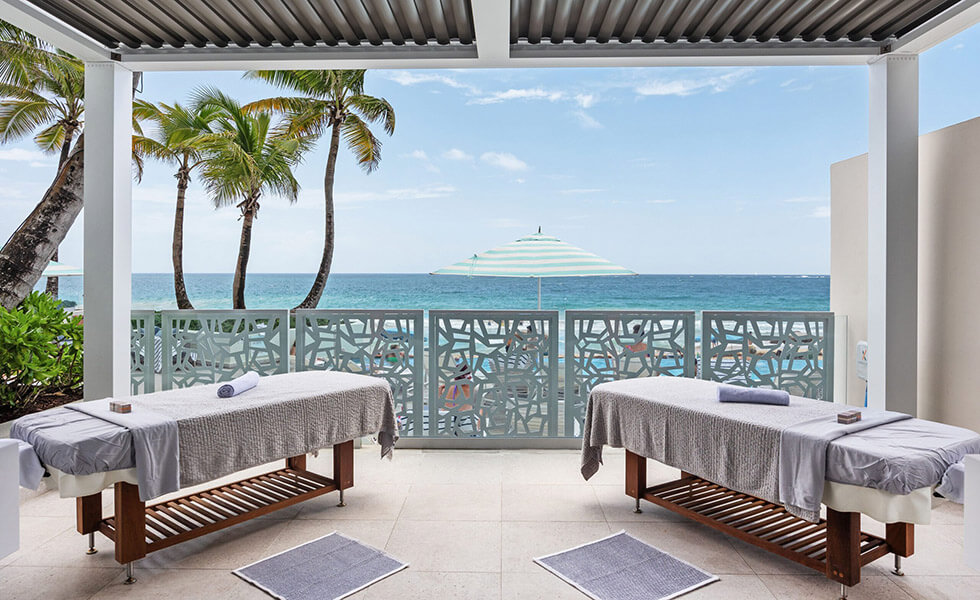 Massage tables on a covered patio overlooking the ocean and some palm trees