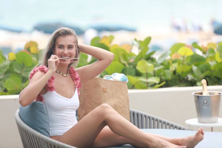 Woman holding onto her sunglasses while lounging on a daybed