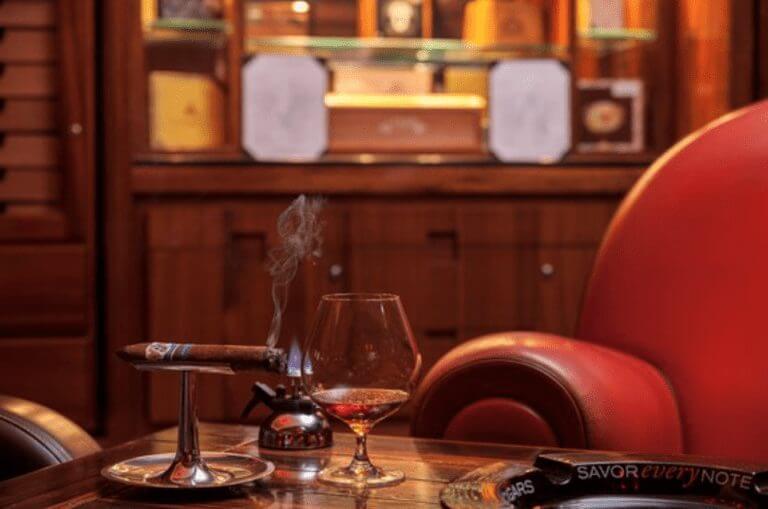 Cigar on a silver holder with an ash catcher and a dark liquor pairing