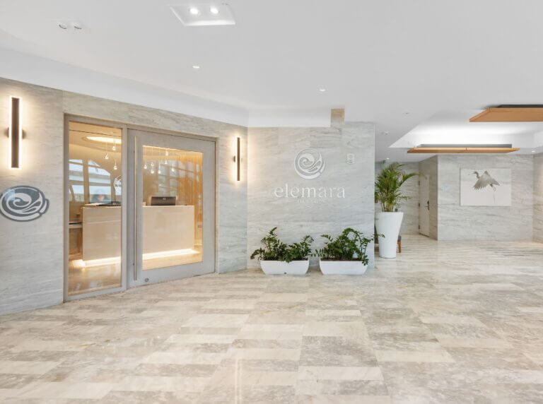 Elemara entrance with simple sconce lighting, beige stone floors, and floor plants