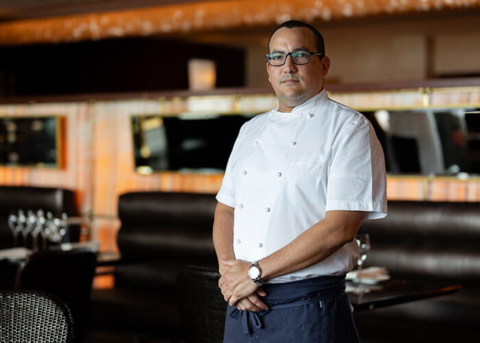 Chef Sebastián Rosado Rivera in a short sleeve chef uniform, glasses, and an apron