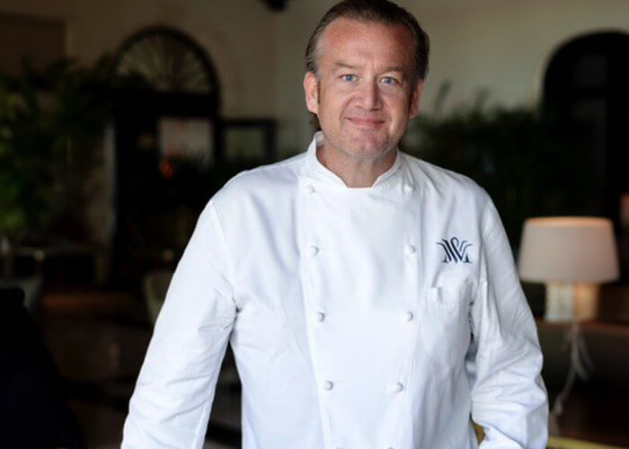 Chef Michael White in a long-sleeve chef uniform smiling slightly
