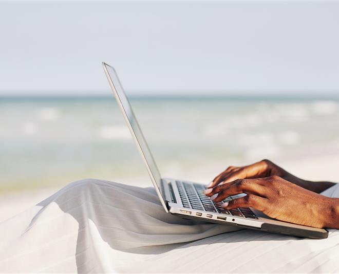 Woman sitting on the beach and typing on laptop