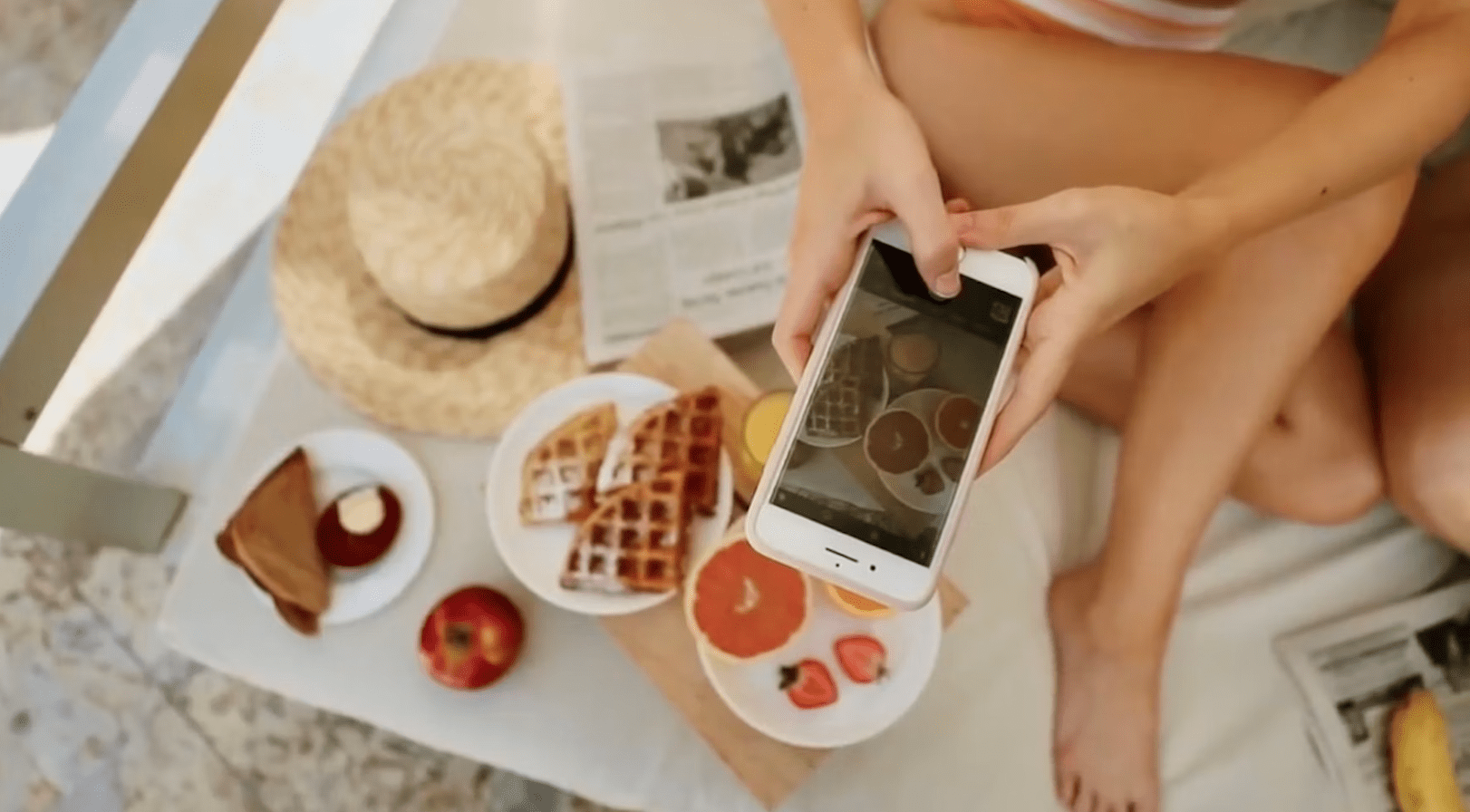 Hand taking a picture of food plates, waffles, fruits and a hat. Cabana tea package at la concha resort