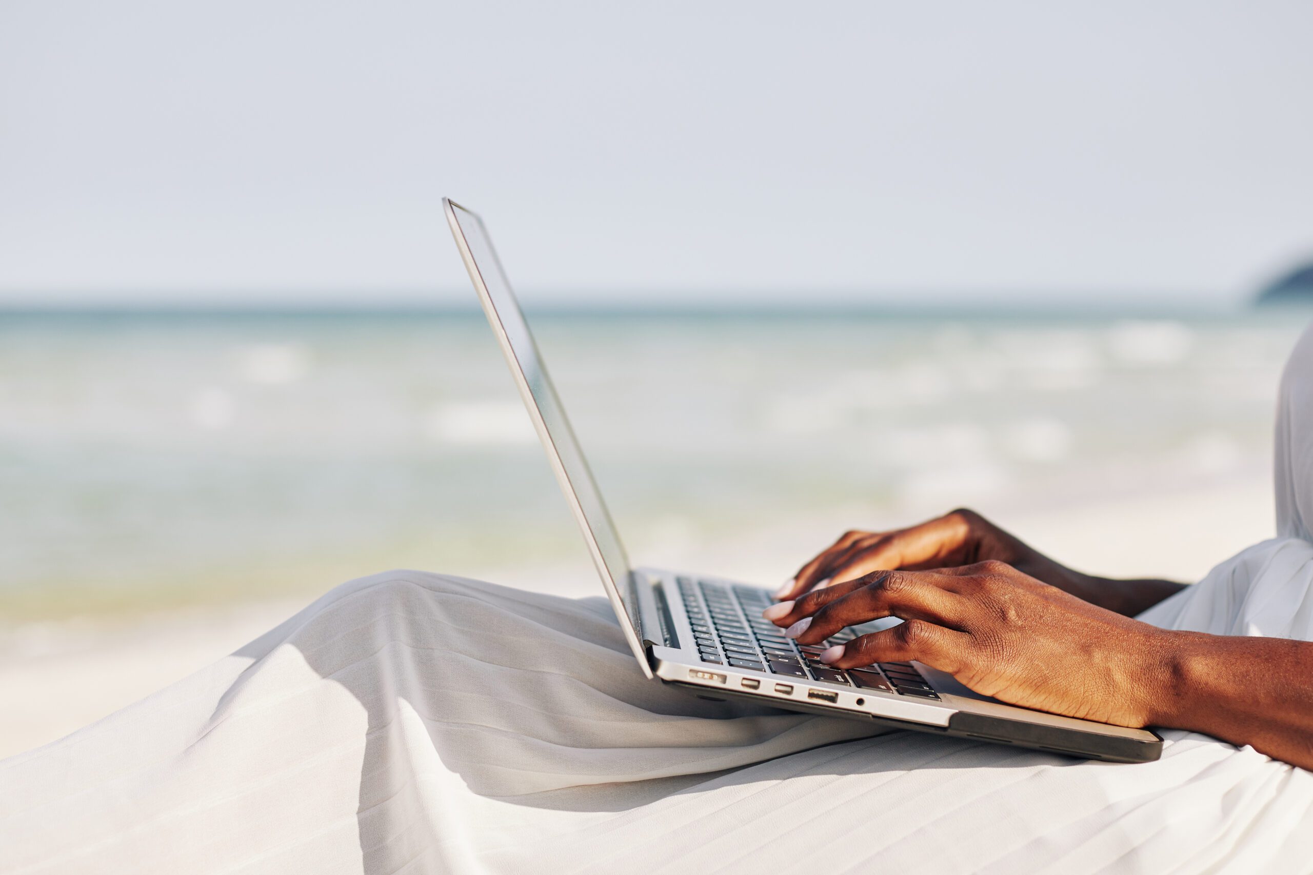 person writing on laptop keyboard at the beach